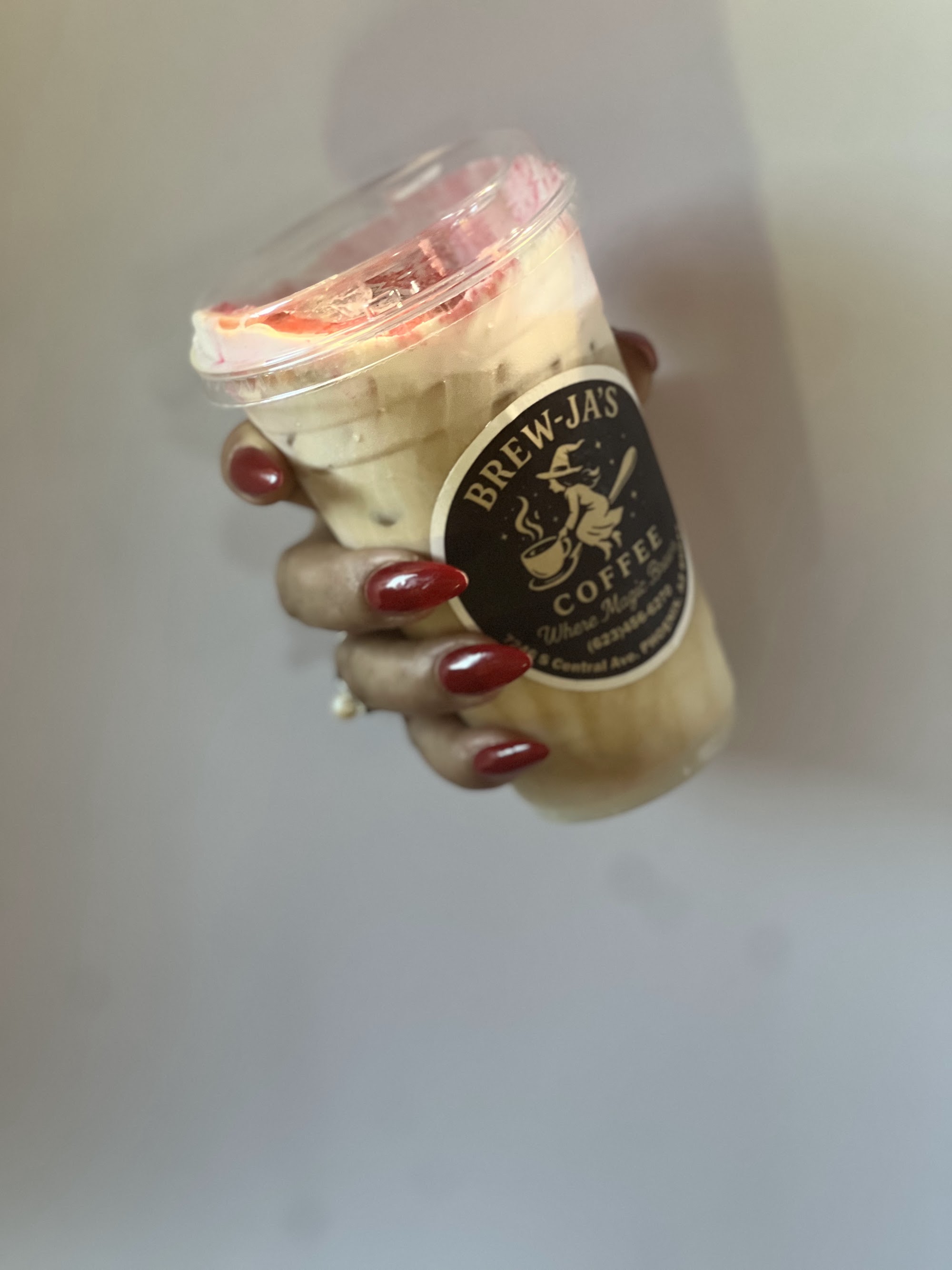 Iced latte with strawberry cold foam in Brew-Ja's cup held by hand with red nail polish