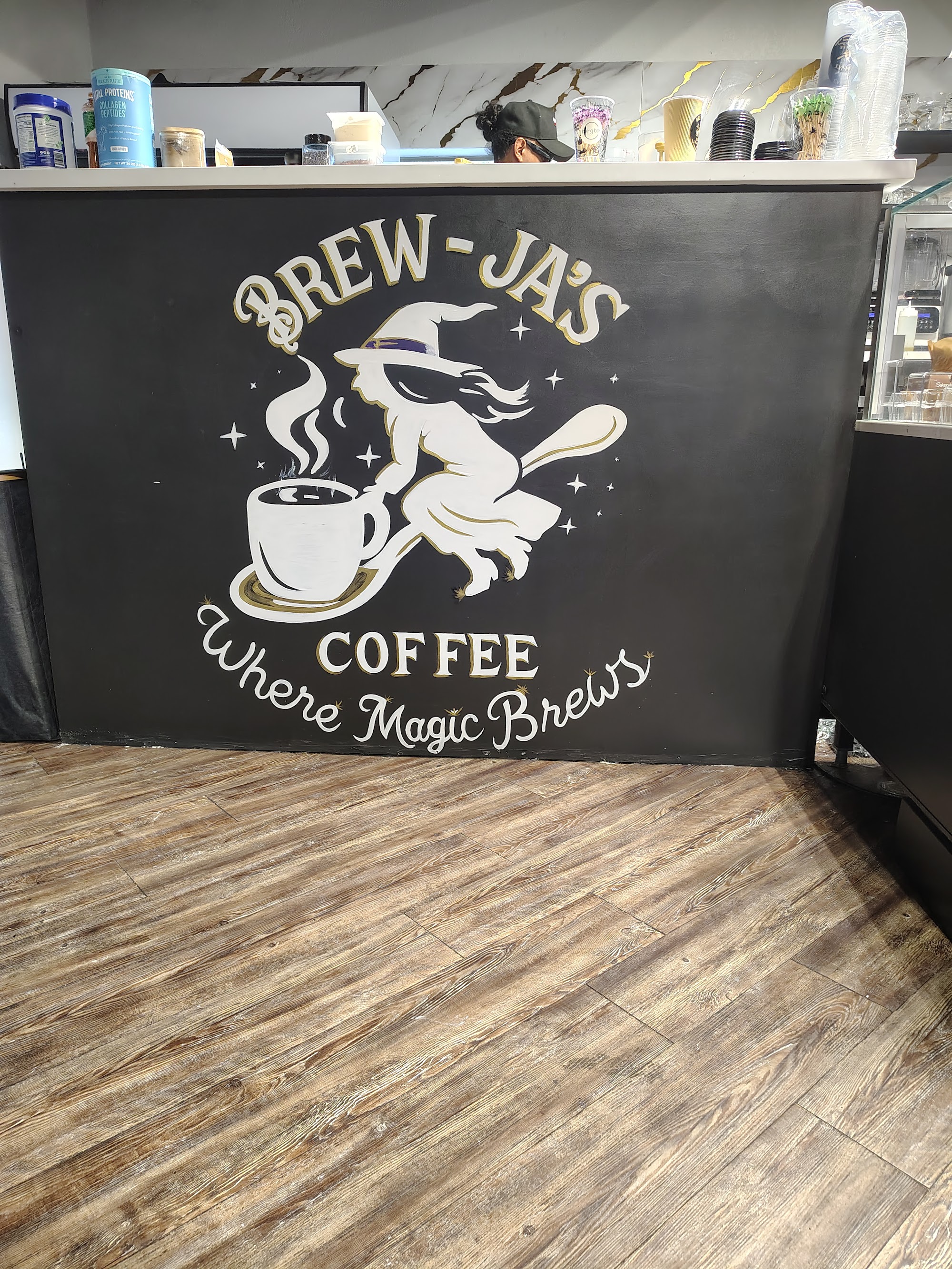 Counter close-up with witch logo, barista, and pastry case visible to the right