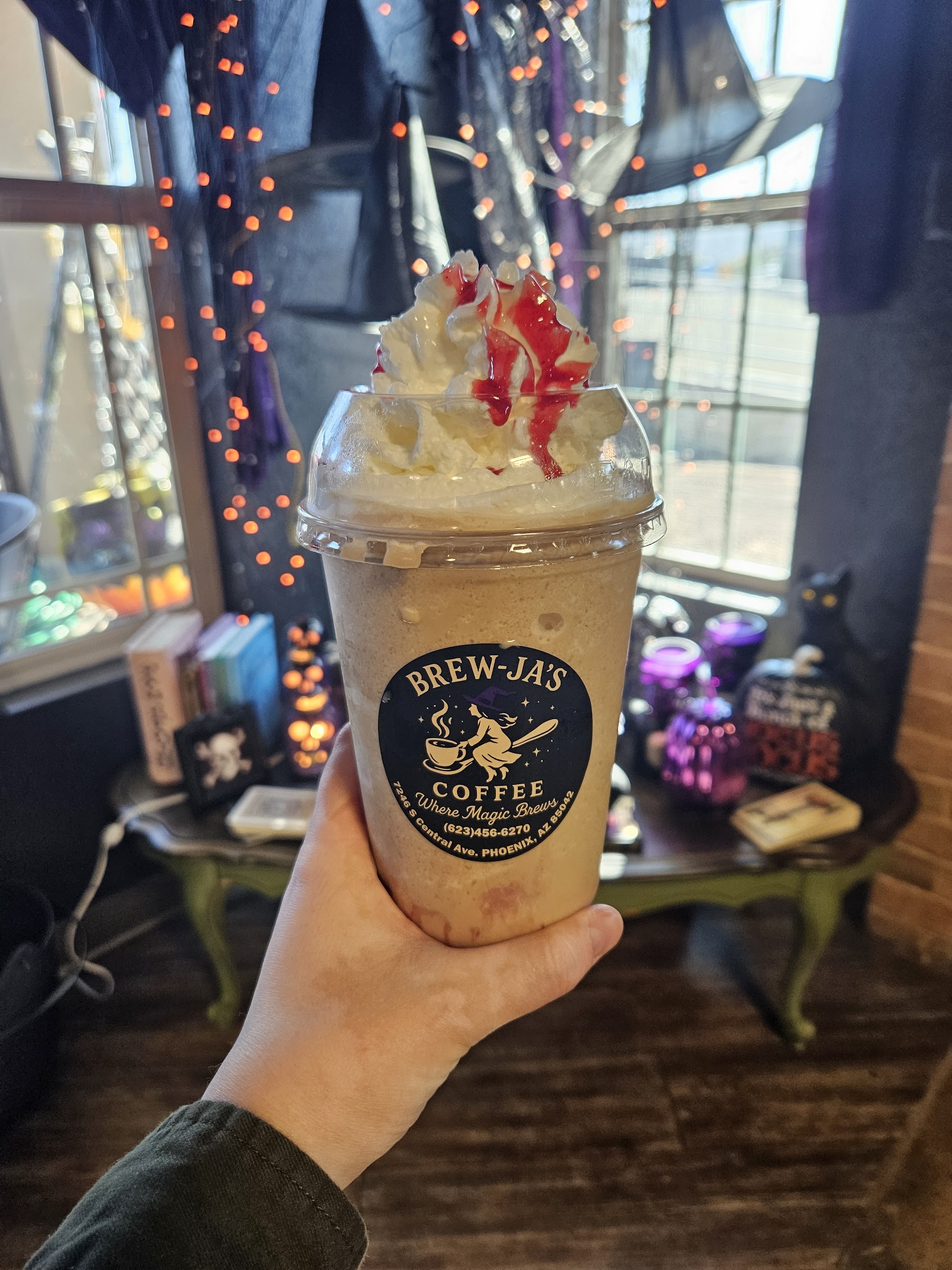 Frappuccino with whipped cream and cherry drizzle held in hand, fairy lights in background