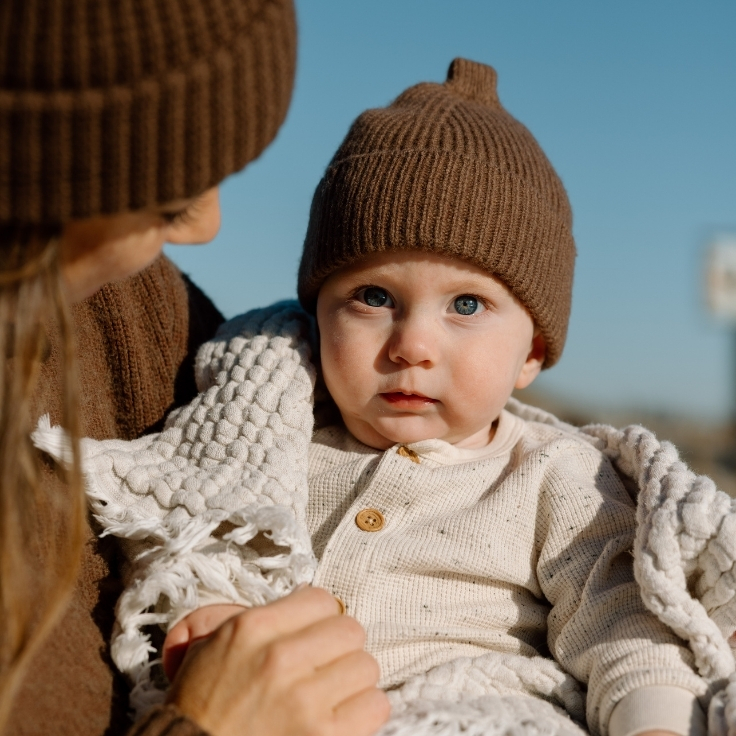 Close-up of a baby wrapped in a cozy blanket during a winter beach family session, with soft light, soulful blue eyes, and coastal tones.