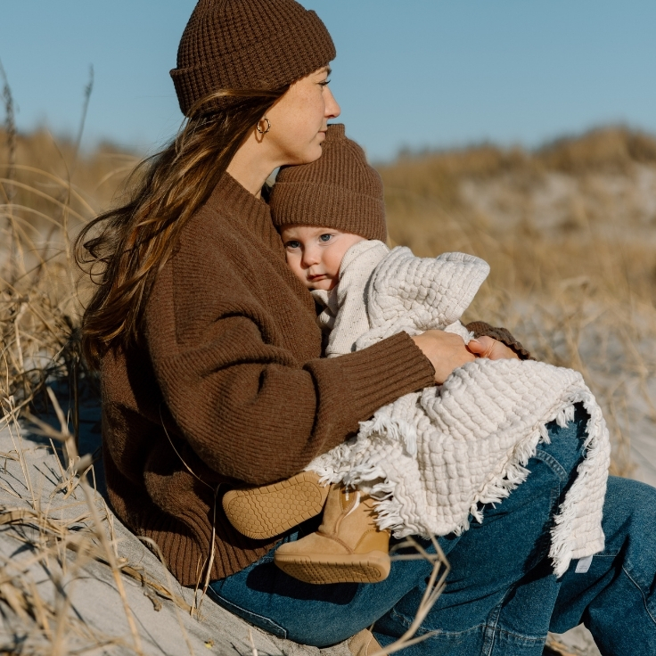 Quiet, intimate moment of a mother holding her baby wrapped in a blanket during a winter beach family session in the dunes.