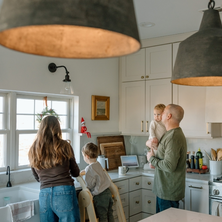 Family of four gathered in the kitchen during a lifestyle family session, making hot cocoa by the window in natural light.