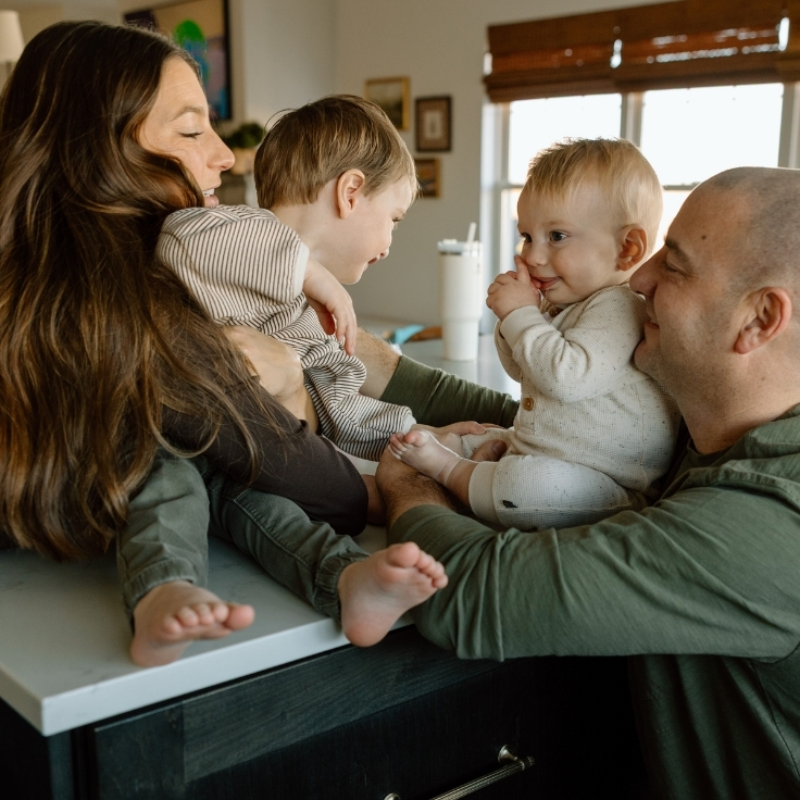 Parents and children cuddled together on the kitchen counter during a cozy in-home family session, sharing playful connection.