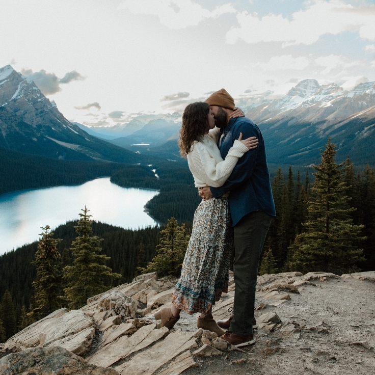 Couple embracing at a mountain overlook above Peyto Lake with sweeping alpine views and turquoise water during a cinematic Banff engagement session.