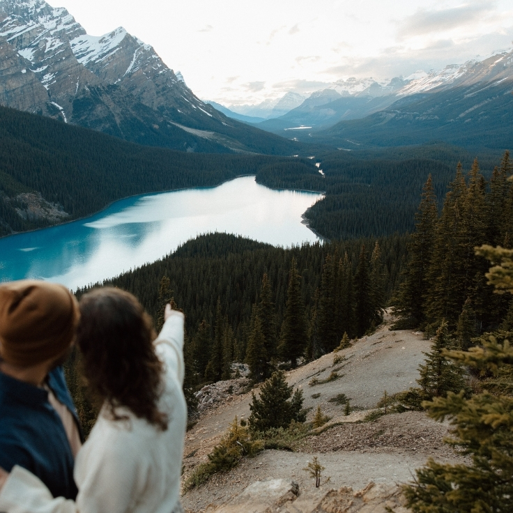 Couple overlooking the turquoise waters of Peyto Lake pointing to the wolf-like shape during sunset with sweeping mountain views and evergreen forests in Banff National Park.