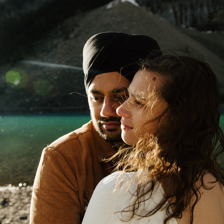 Close-up engagement portrait of a couple embracing beside the turquoise waters of Moraine Lake during sunset in Banff, Alberta.