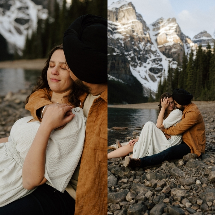 Intimate lakeside engagement portraits of a couple cuddling on the rocky shoreline beneath snow-capped mountains during a cinematic Banff engagement session in Alberta, Canada.