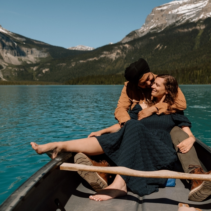 Couple cuddling in a canoe on a turquoise alpine lake surrounded by mountain views during a romantic engagement session in Yoho National Park, Canada.