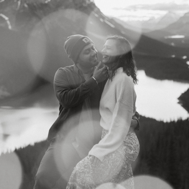 Black and white engagement portrait of a couple laughing together at a scenic overlook above Peyto Lake in the Canadian Rockies.