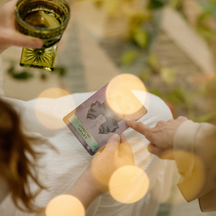 A client and spiritual facialist explore an oracle card together over herbal tea as part of an intentional self-care and energy healing ritual. A client and spiritual facialist explore an oracle card together over herbal tea as part of an intentional self-care and energy healing ritual.