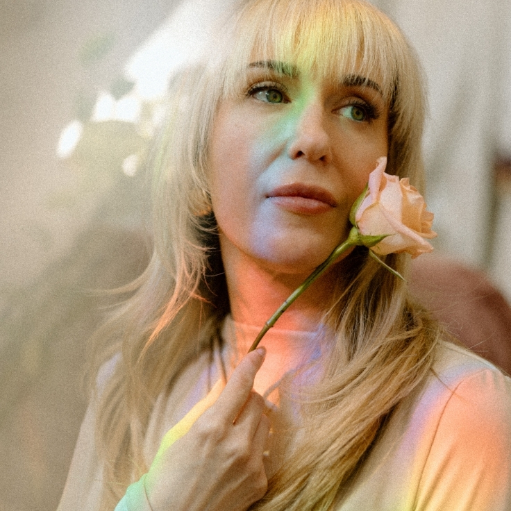 A dreamy portrait of a spiritual facialist holding a rose with soft rainbow prism light reflects the beauty, mindfulness, and artistry behind holistic skincare. A dreamy portrait of a spiritual facialist holding a rose with soft rainbow prism light reflects the beauty, mindfulness, and artistry behind holistic skincare.