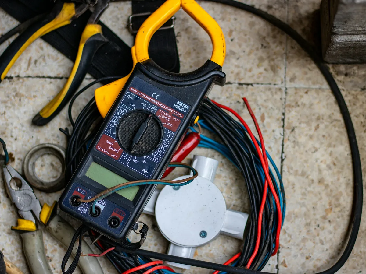Electrician's clamp meter, pliers and cable on a floor