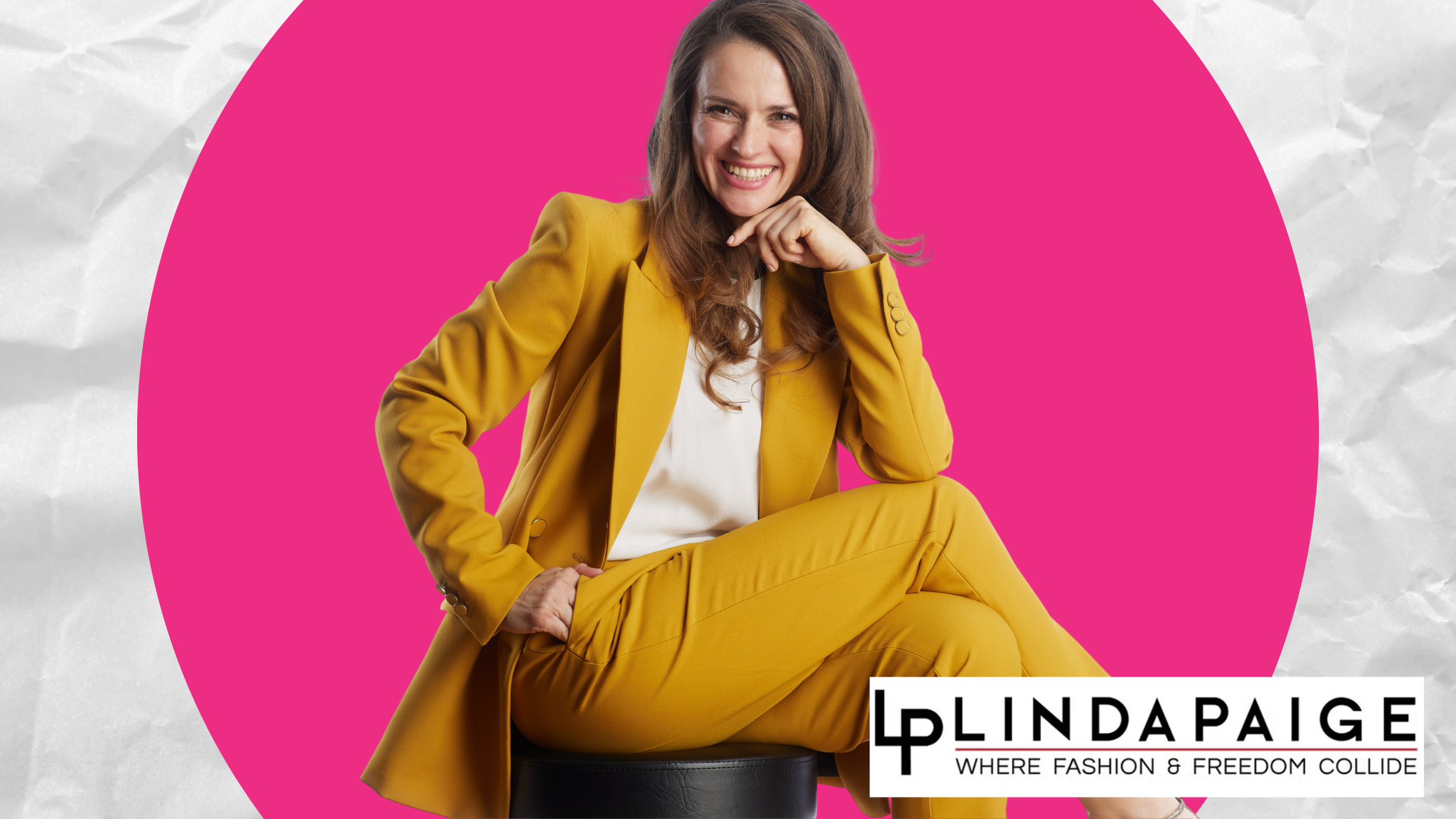 onfident woman seated in a mustard suit smiling on a pink background