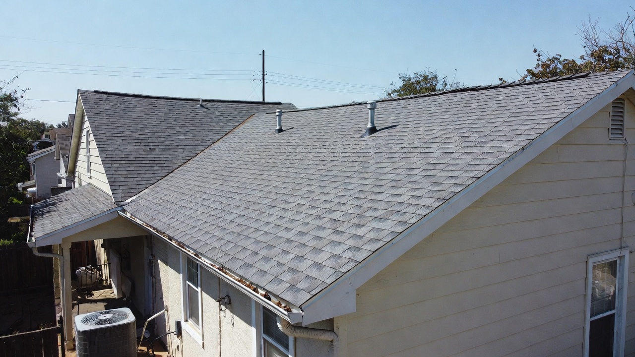 Drone aerial view of a residential asphalt shingle roof with gray shingles, roof vents, and gutters