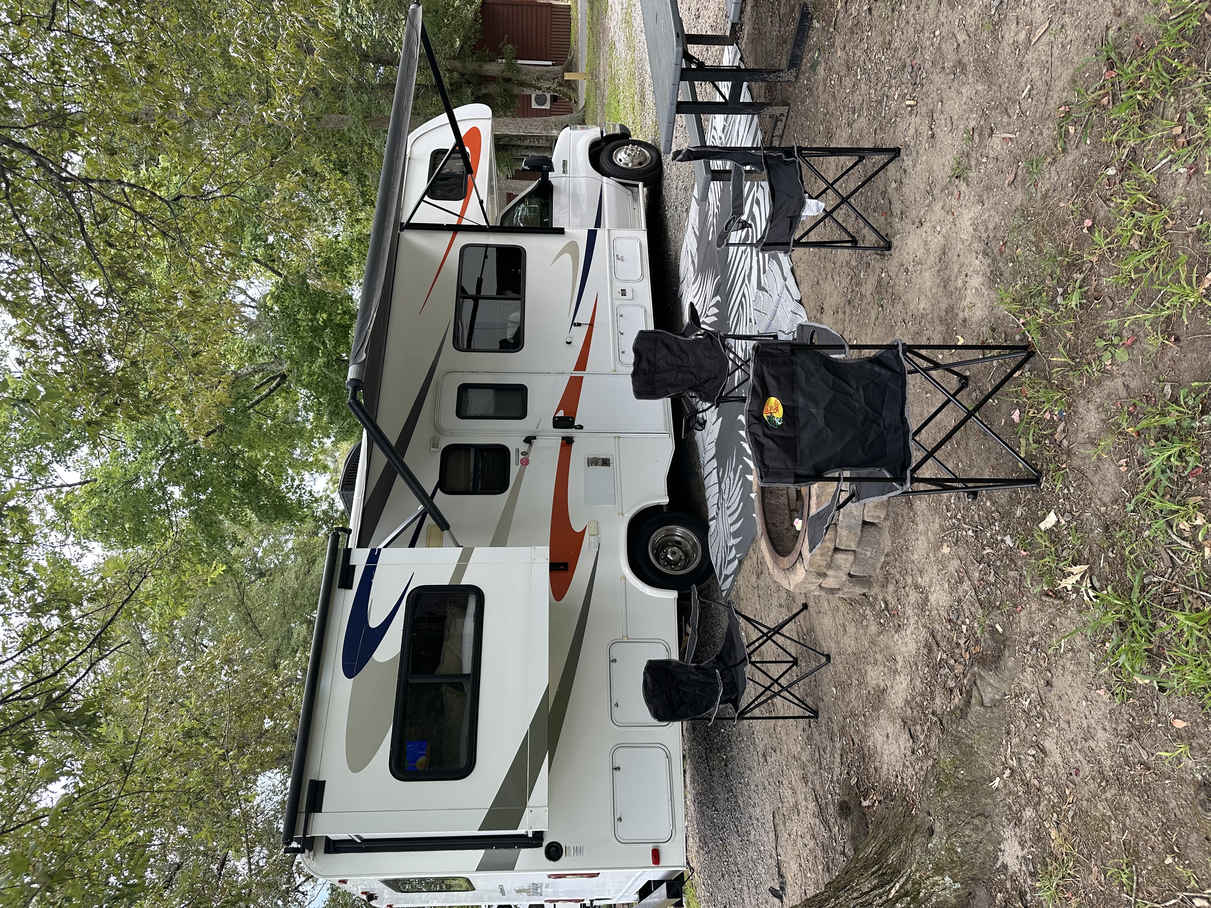 2016 Forest River Sunseeker 2700DS Ford Class C RV parked at a campsite with awning extended, outdoor chairs, picnic table, and fire pit.
