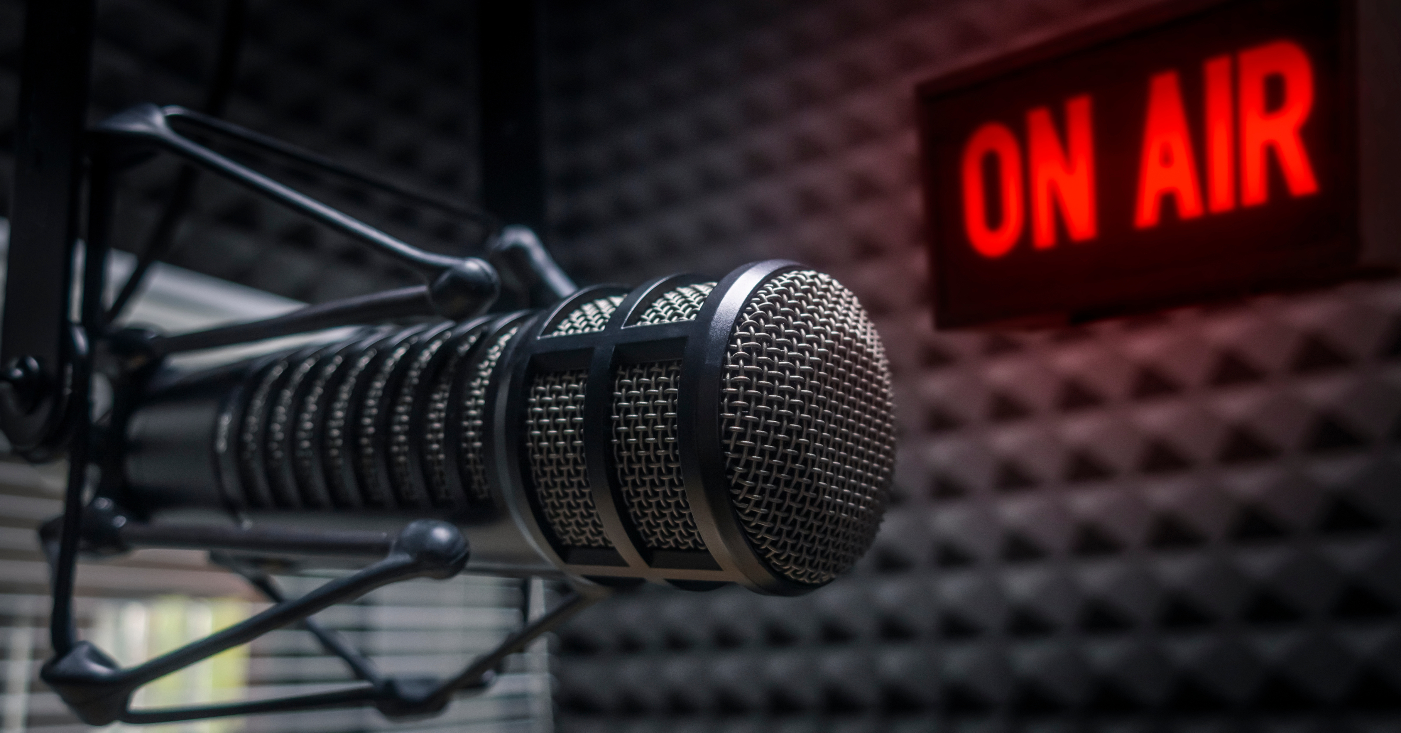 Close-up of a studio microphone with a glowing “On Air” sign in the background, representing a podcast or radio broadcast.
