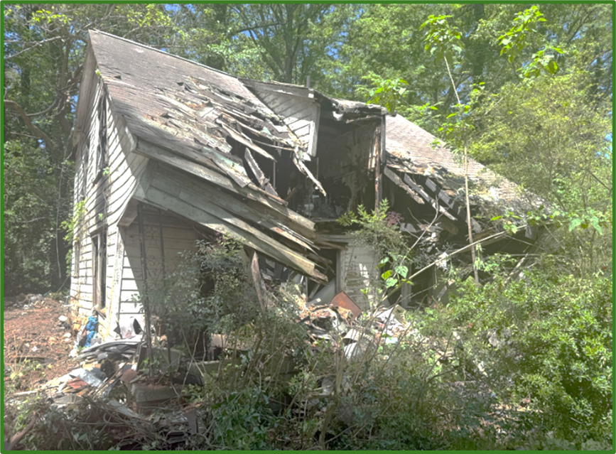 Severely deteriorated house at 666 Sheppard Road with a collapsed roof, exposed interior, and dense overgrowth, illustrating unsafe conditions before demolition.