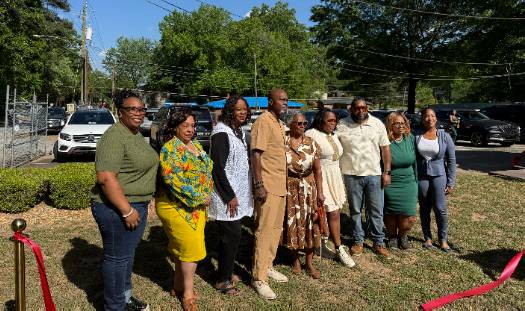 Group of family, friends, community members, and local officials pose together at the Arthur J. Queen Drive unveiling ceremony, standing outdoors near the ribbon-cutting area, with Commissioner Chakira Johnson at the far left.