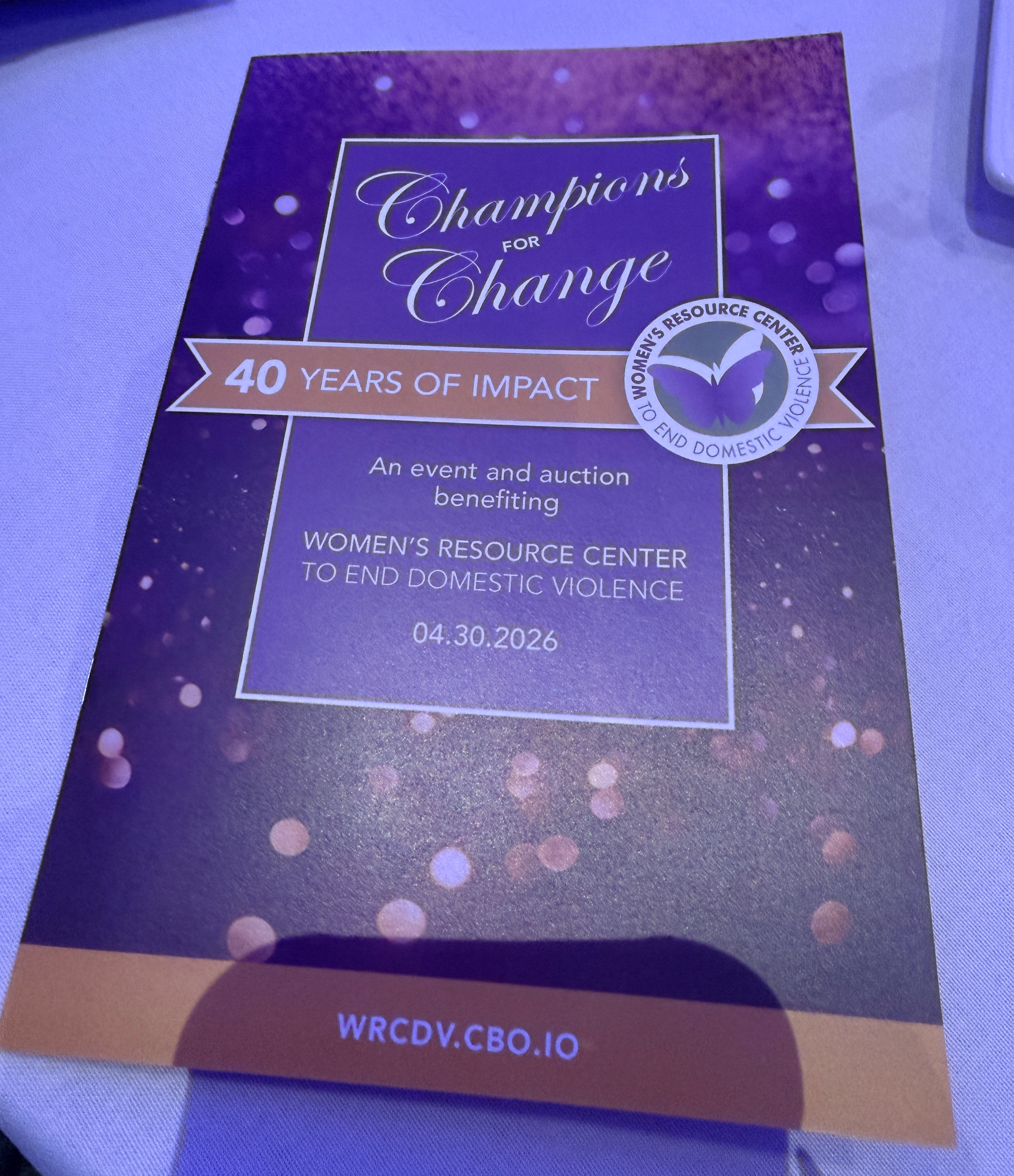 Program booklet for the Women’s Resource Center to End Domestic Violence’s “Champions for Change” event celebrating “40 Years of Impact.” The purple and gold booklet includes the organization’s butterfly logo and text reading: “An event and auction benefiting Women’s Resource Center to End Domestic Violence,” dated April 30, 2026. Website listed at the bottom: wrcdv.cbo.io.
