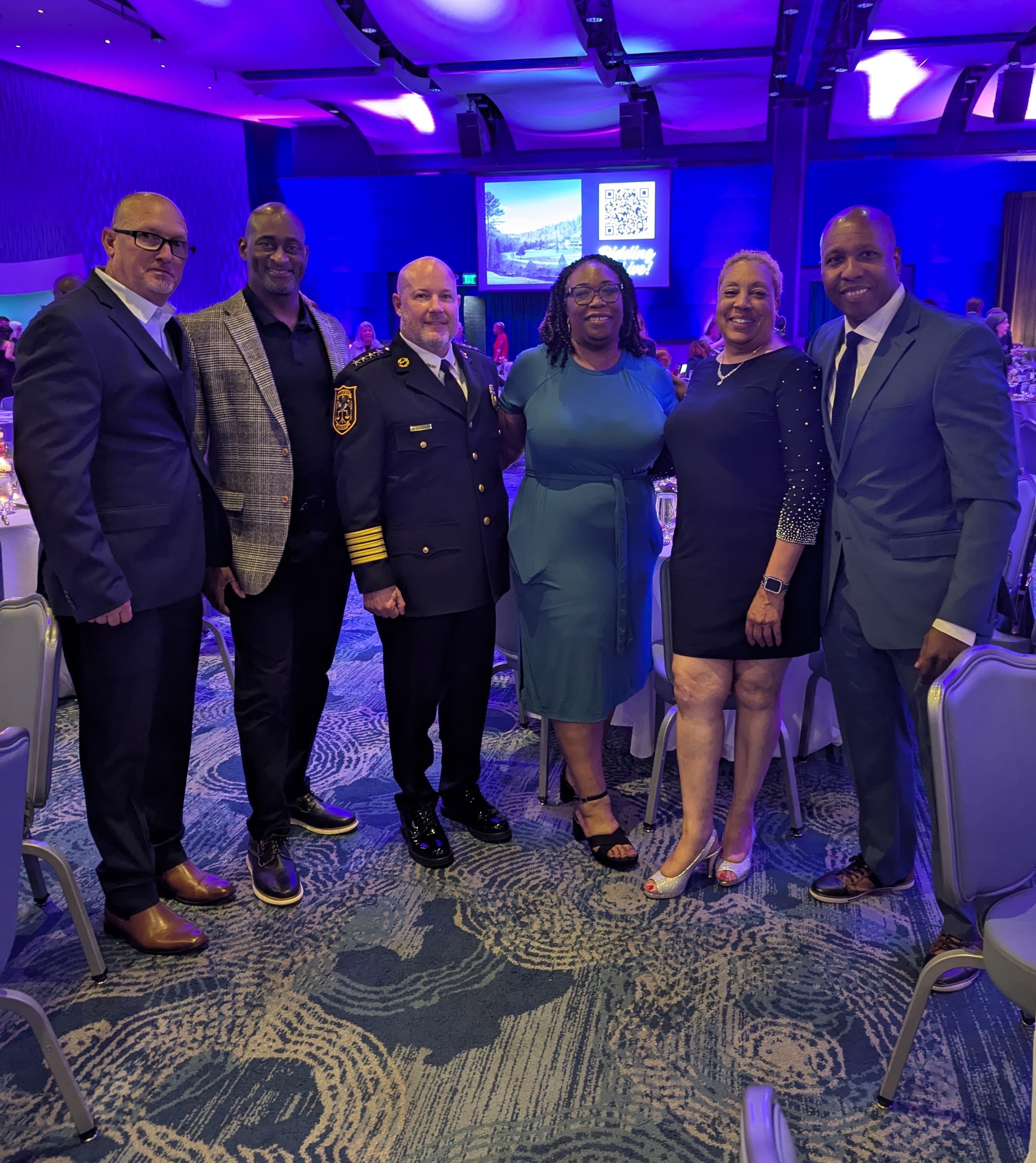Group photo taken during the Champions for Change Gala featuring DeKalb County public safety and government leaders standing together in a ballroom with purple and blue lighting. From left to right are DeKalb Marshal Kevin Richardson; DeKalb County School District Police Chief Tracey Whaley; DeKalb Police Chief Gregory Padrick in formal uniform; Presiding Officer Commissioner Chakira Johnson wearing a teal dress; Executive Administrator for the DeKalb Clerk of Superior Court Laveeta Branche; and Stone Mountain Police Chief James Westerfield. Banquet tables and a projection screen are visible in the background.