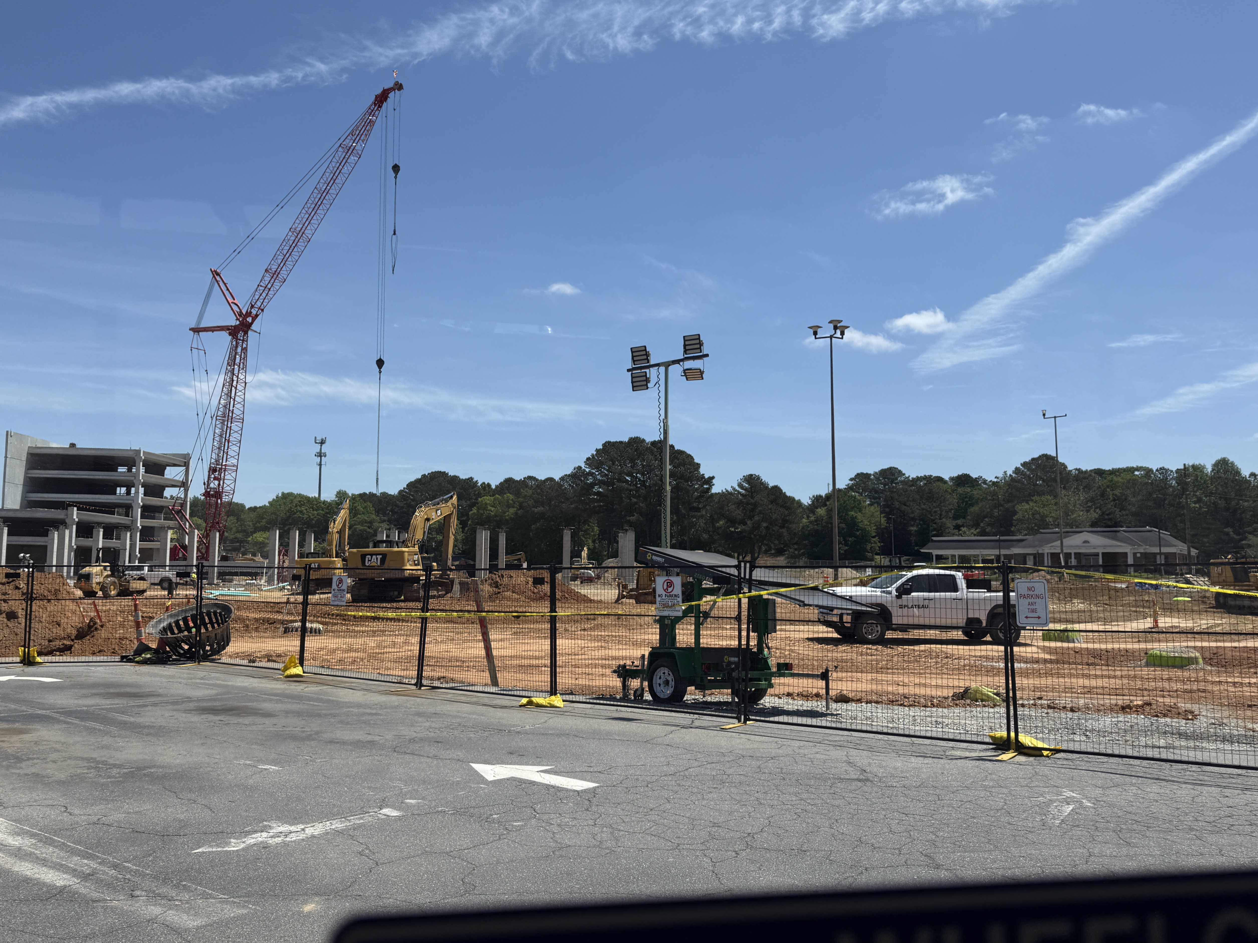View of ongoing construction at the future Lulah Hills development site. A large crane, excavators, construction fencing, and partially completed structures are visible beneath a bright blue sky during the guided site tour.