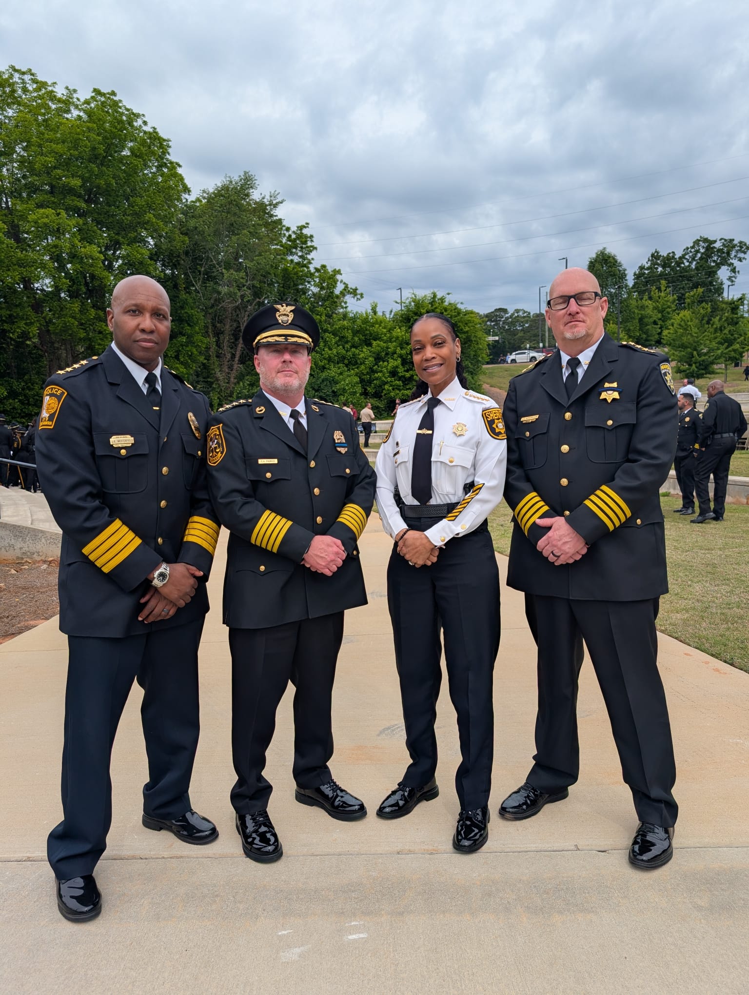 From left: City of Stone Mountain Police Chief James Westerfield, DeKalb County Police Chief Gregory Padrick, DeKalb Sheriff Melody Maddox, and DeKalb Marshal Kevin Richardson pose together outdoors during the Fallen Officers Memorial Ceremony. The four public safety leaders wear formal dress uniforms and stand near the ceremony site with attendees and trees visible in the background beneath an overcast sky.