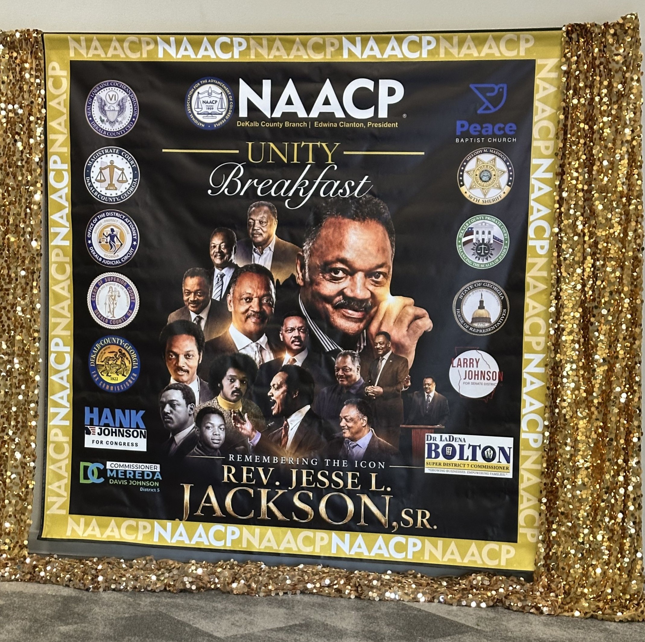 Decorative display backdrop at the NAACP DeKalb County Branch Unity Breakfast honoring the legacy of Rev. Jesse L. Jackson Sr. The display features multiple portraits of Jackson throughout his life and career, surrounded by NAACP branding, sponsor logos, and gold sequin accents framing the backdrop.