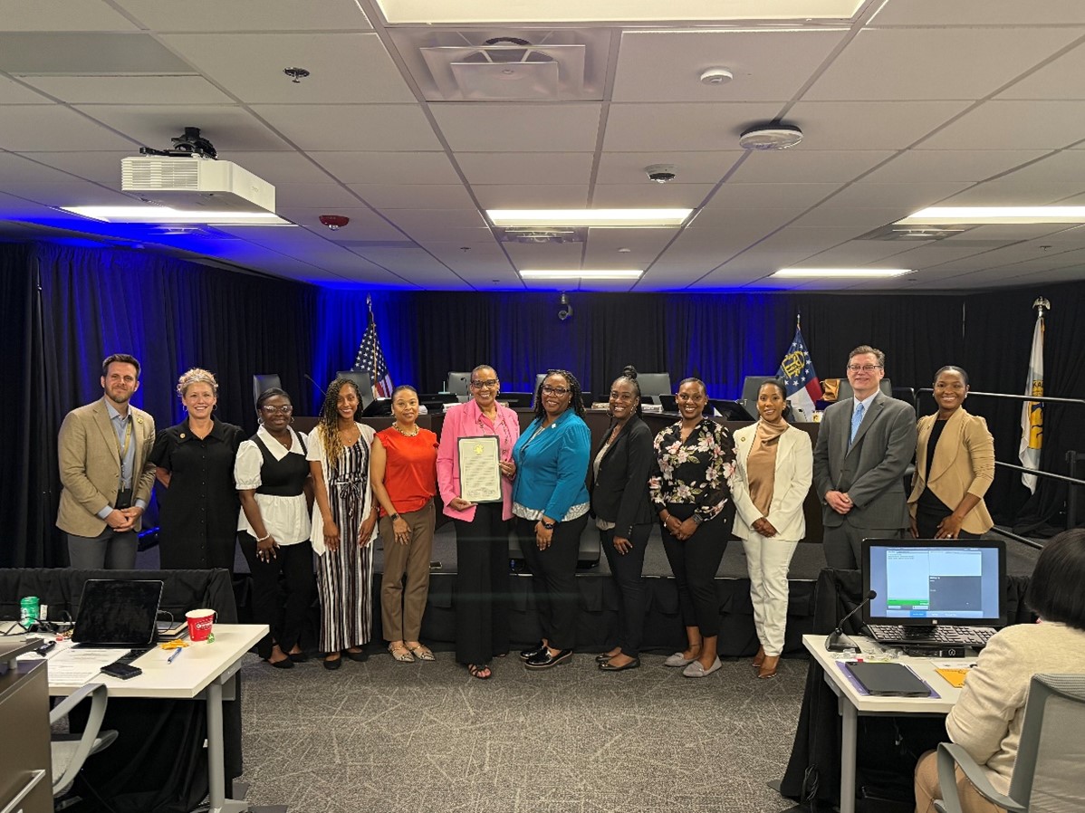 Group photo inside a DeKalb County Board of Commissioners meeting room. Super District 6 Commissioner Ted Terry, District 2 Commissioner Michelle Long Spears, Dr. Asia Foster, Erika Cotton, Jacquelyn E. Bridges, Dr. Sedessie Spivey, Presiding Officer Commissioner Chakira Johnson, Stefani Carter, Dr. Christiana Johnson, District 3 Commissioner Nicole Massiah, District 1 Commissioner Robert Patrick, and Deputy Presiding Officer Super District 7 Commissioner Dr. LaDena Bolton stand together following a proclamation presentation recognizing DeKalb Public Health. One participant holds a framed proclamation while the group poses in front of the dais.