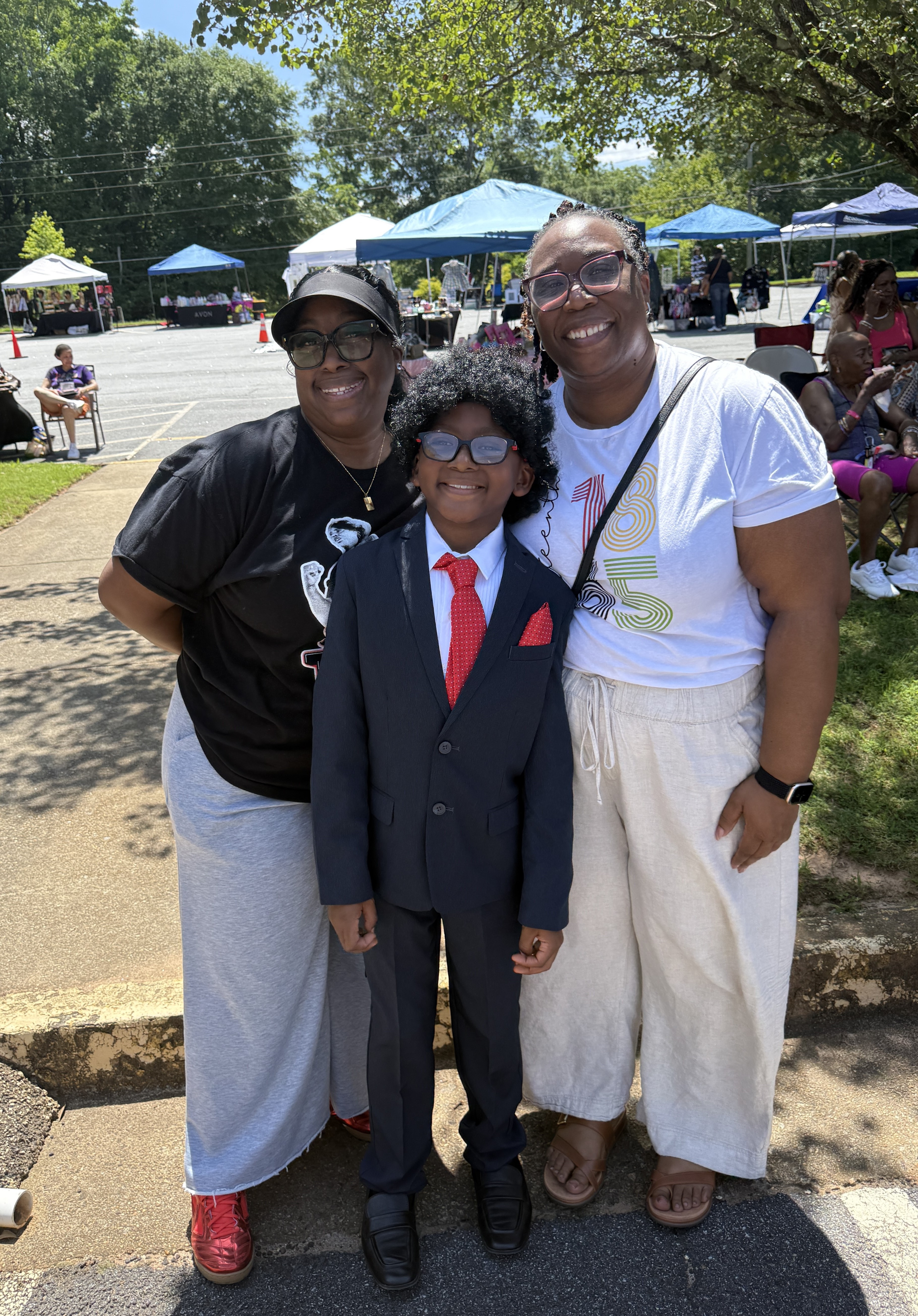 Commissioner Chakira Johnson poses for a photo with a woman and a young participant during the Antioch AME Church Juneteenth Community Event. Vendor tents and attendees are visible in the background.