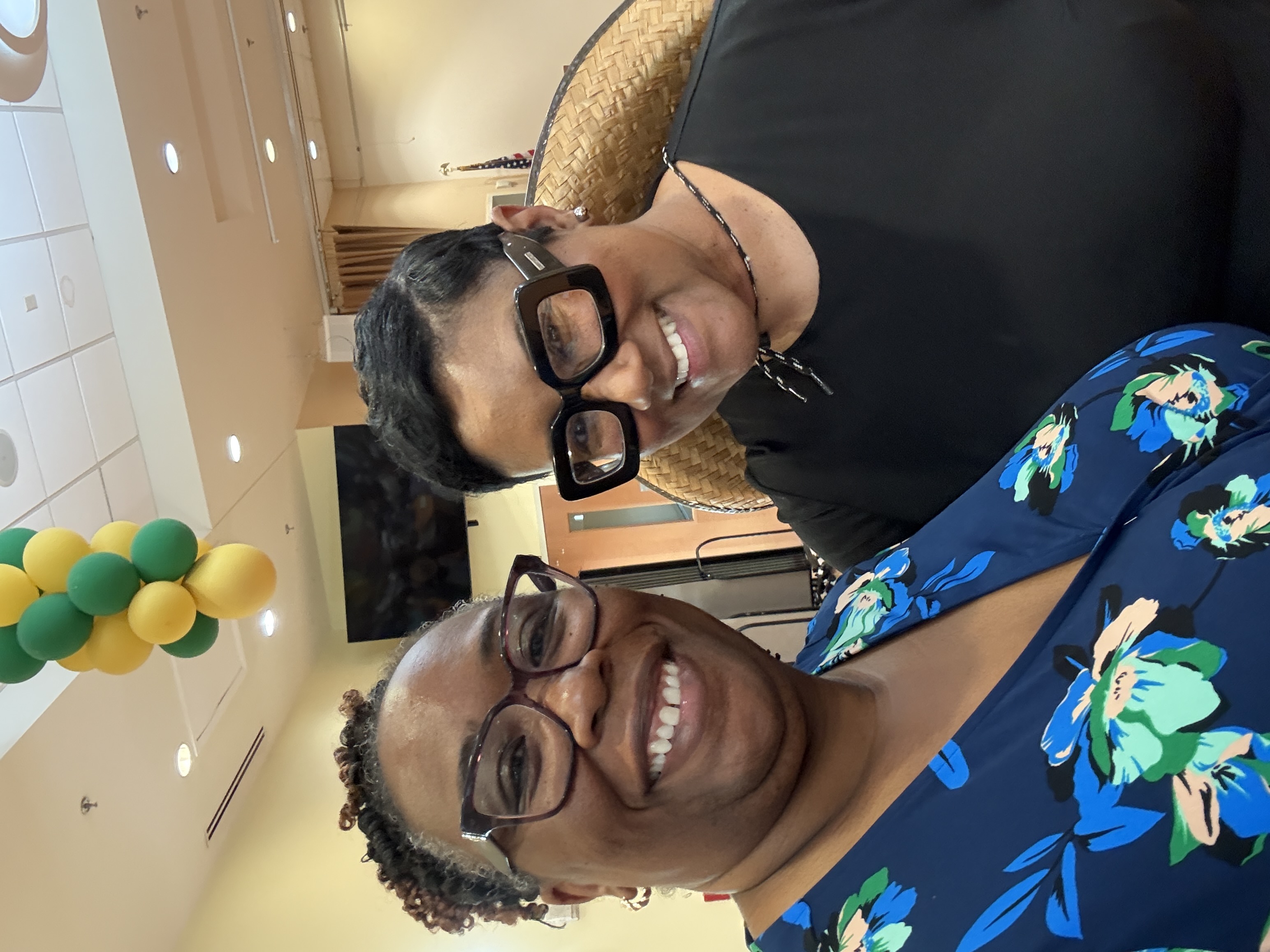 Presiding Officer Commissioner Chakira Johnson poses with CEO Lorraine Cochran-Johnson during the Dancing for Dementia event at the Lou Walker Senior Center. Both smile for the camera inside the decorated event space, with green and yellow balloons visible overhead.