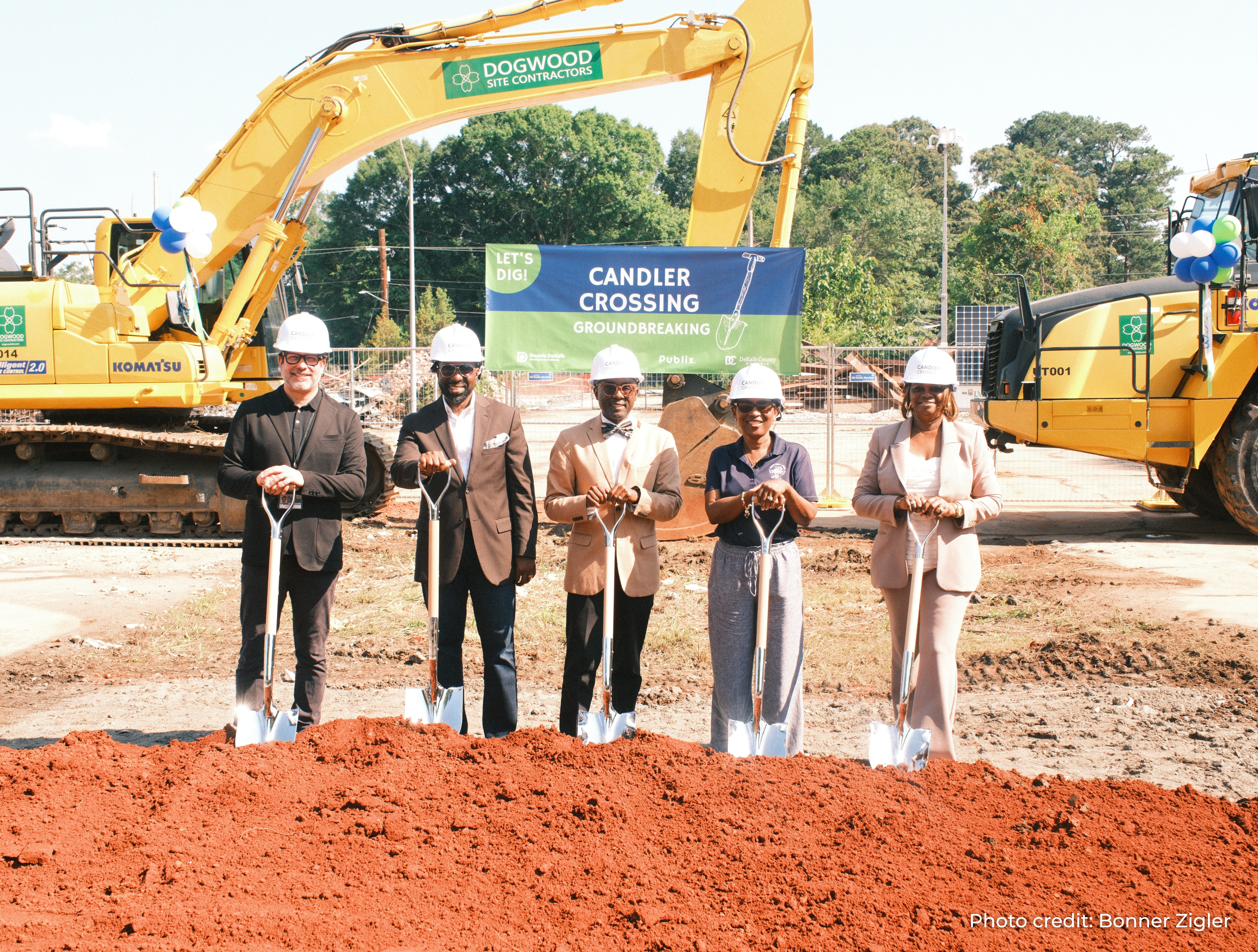District 4 Chief of Staff Alesia Brooks and other project partners pose with ceremonial shovels at the Candler Crossing groundbreaking ceremony. A project sign and large construction equipment are visible behind the group at the future mixed-use development site in South DeKalb. Photo credit: Bonner Zigler.