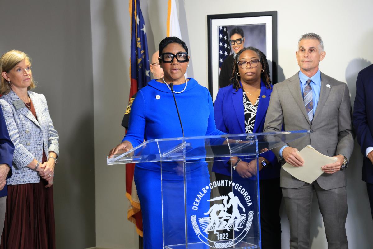 DeKalb County CEO Lorraine Cochran-Johnson speaks at a podium during a press conference announcing a coordinated response to youth violence and the Education to Empowerment initiative, with Presiding Officer Commissioner Chakira Johnson and other County and community leaders standing behind her.