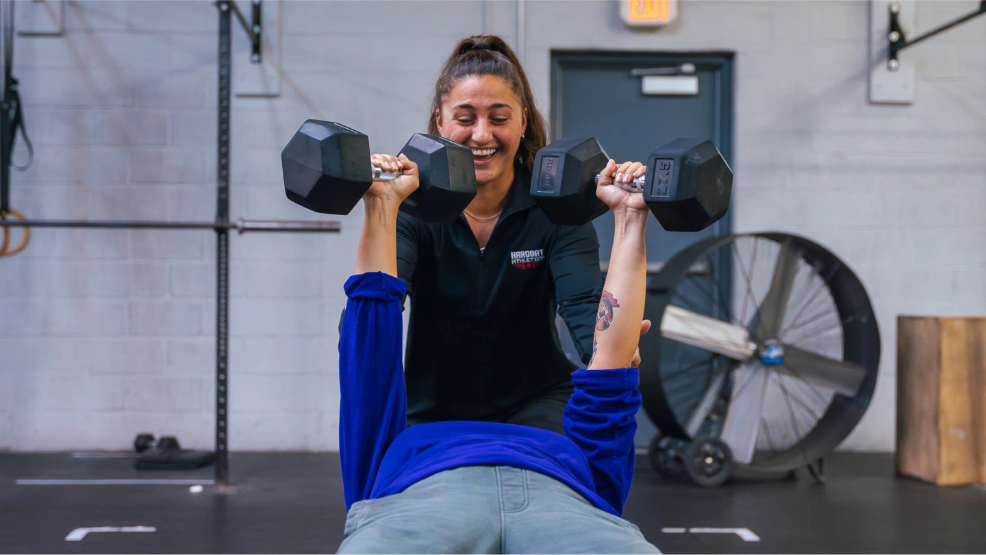 A Hardbat coach guiding a member through a dumbbell press