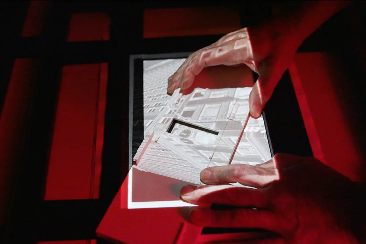 Hands position the Perfect Test Strip Printer over the highlight area of a projected darkroom print on an easel baseboard under red safelight. Hands position the Perfect Test Strip Printer over the highlight area of a projected darkroom print on an easel baseboard under red safelight.