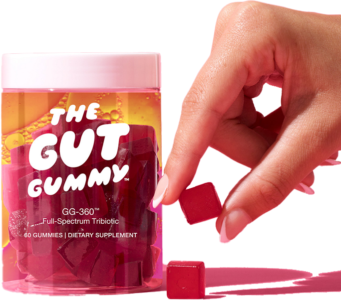 Hand picking a red Gut Gummy from a clear supplement jar labeled “The Gut Gummy™ – GG-360™ Full-Spectrum Tribiotic, 60 Gummies.”