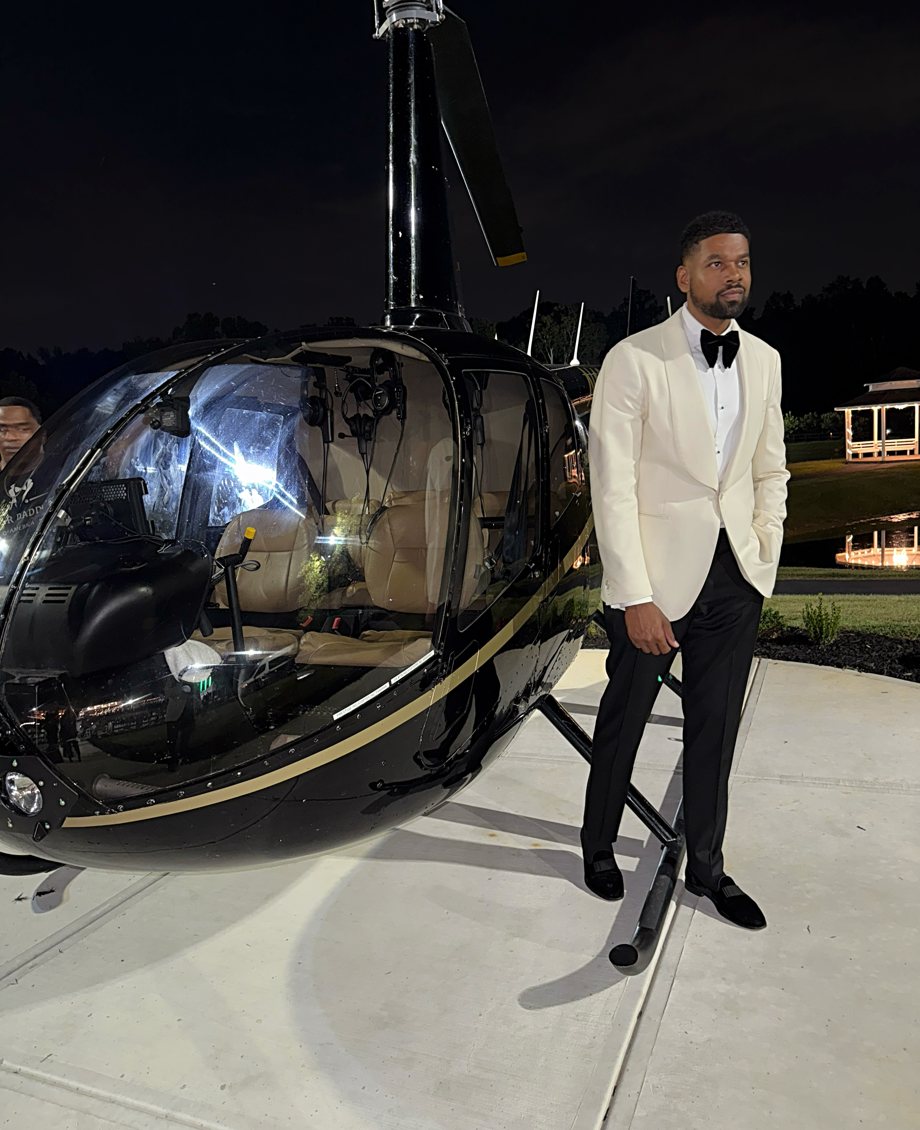 Brock in a white dinner jacket beside a helicopter at night