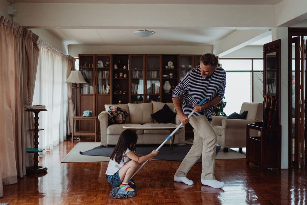 Father and daughter cleaning the living room floor together during a fall home reset