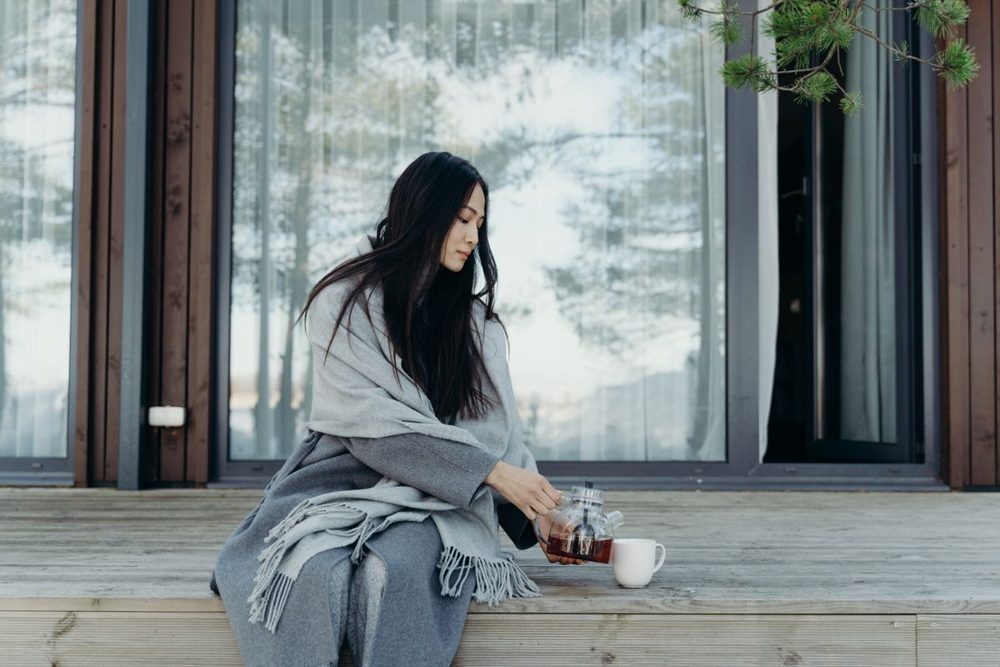 Woman wrapped in a blanket relaxing with tea on a porch, taking a quiet moment for herself