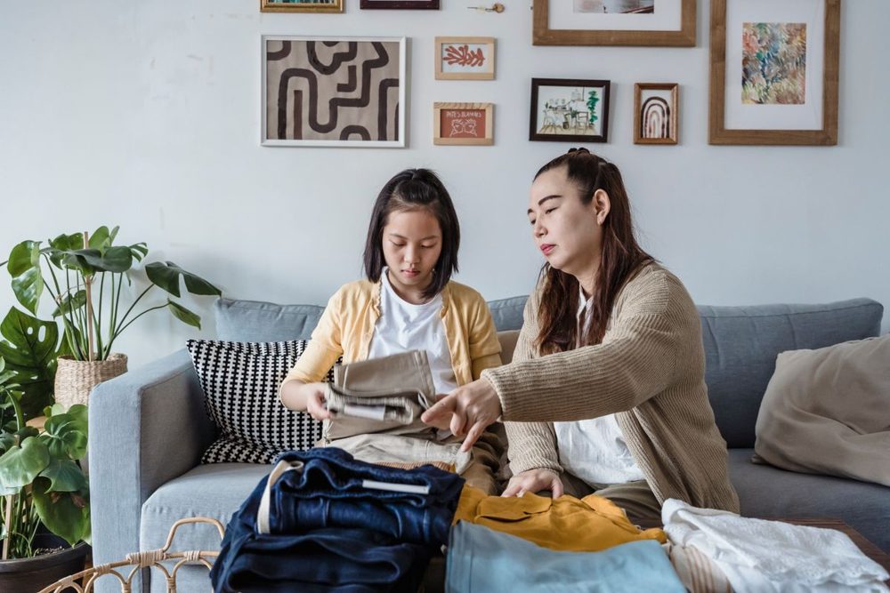 Mother and daughter sorting and folding seasonal clothing together on the couch