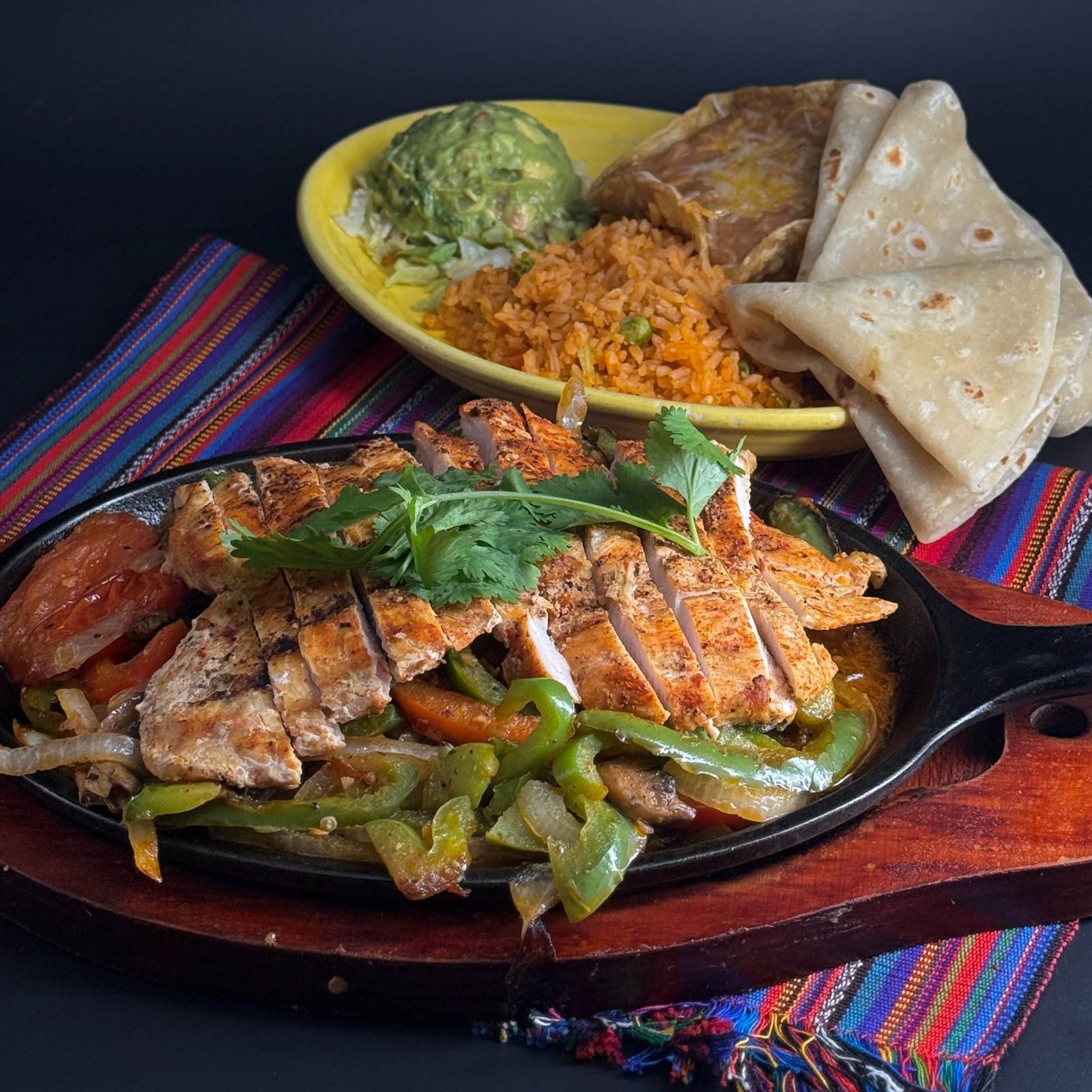 Grilled chicken fajitas on a sizzling skillet with peppers and onions, with guacamole, rice and flour tortillas at Casa de Bandini, Carlsbad