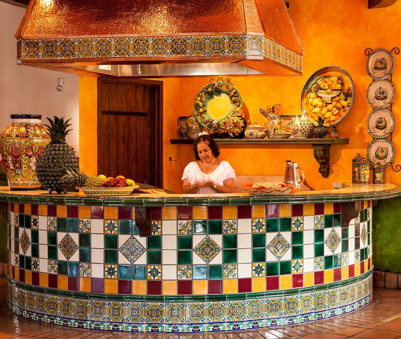 Copper hood and curved hand-painted tile counter of the Casa de Bandini tortilla station, with a cook behind, Carlsbad