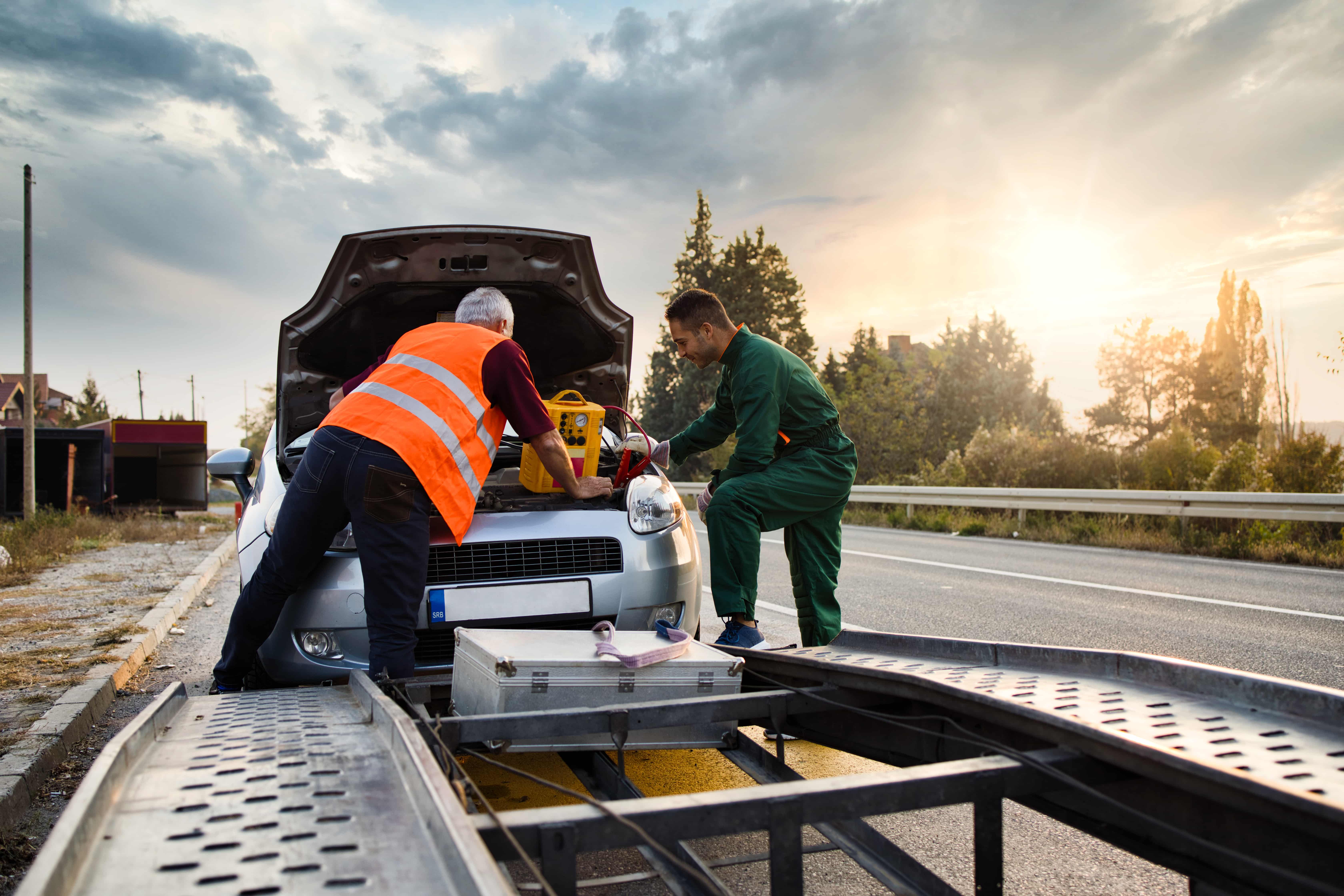 two male technicians loading a car onto a flatbed