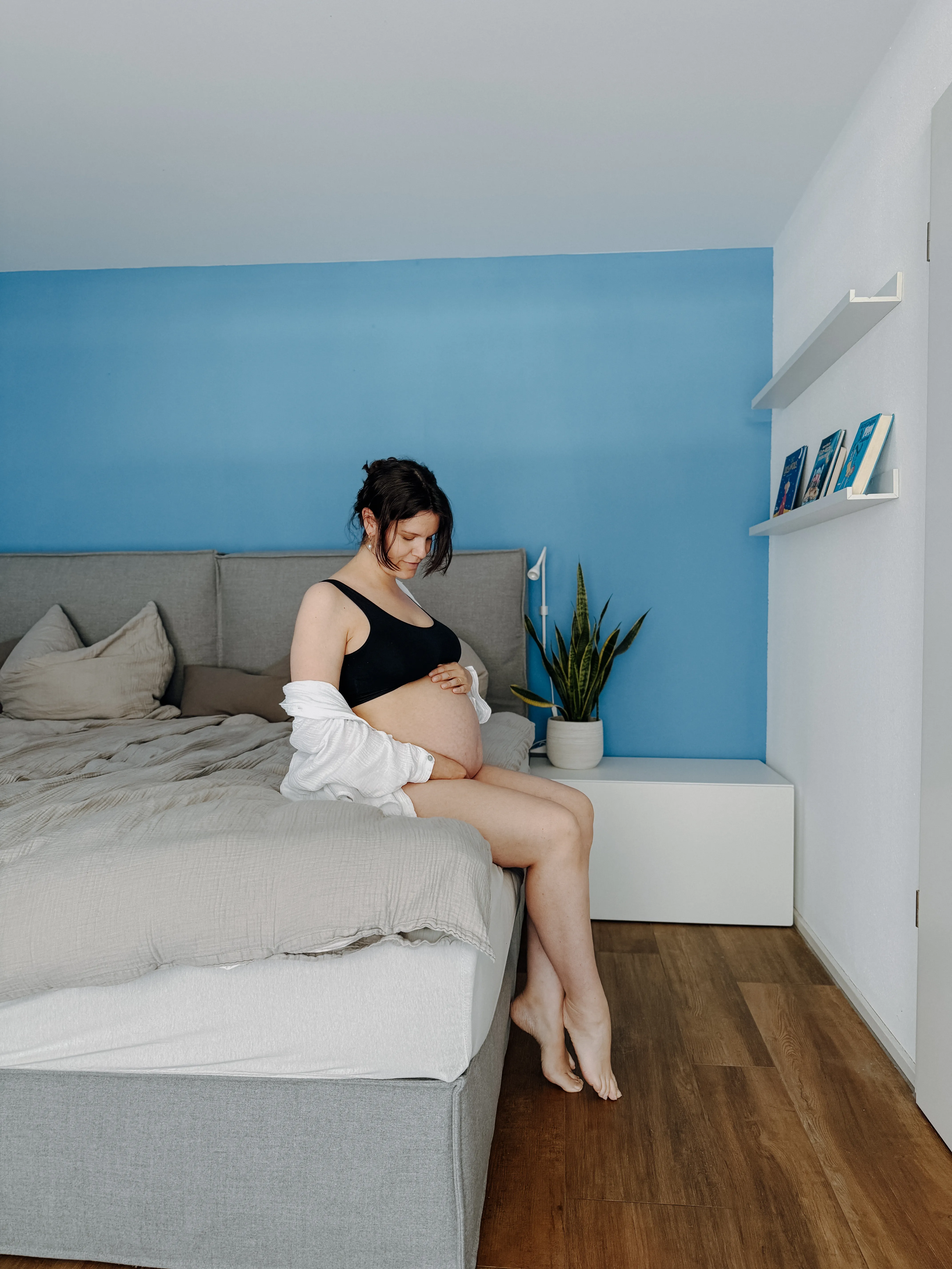 Seitlich am Fenster stehend, die Hände gefaltet unter dem Bauch, ruhiger Ausdruck