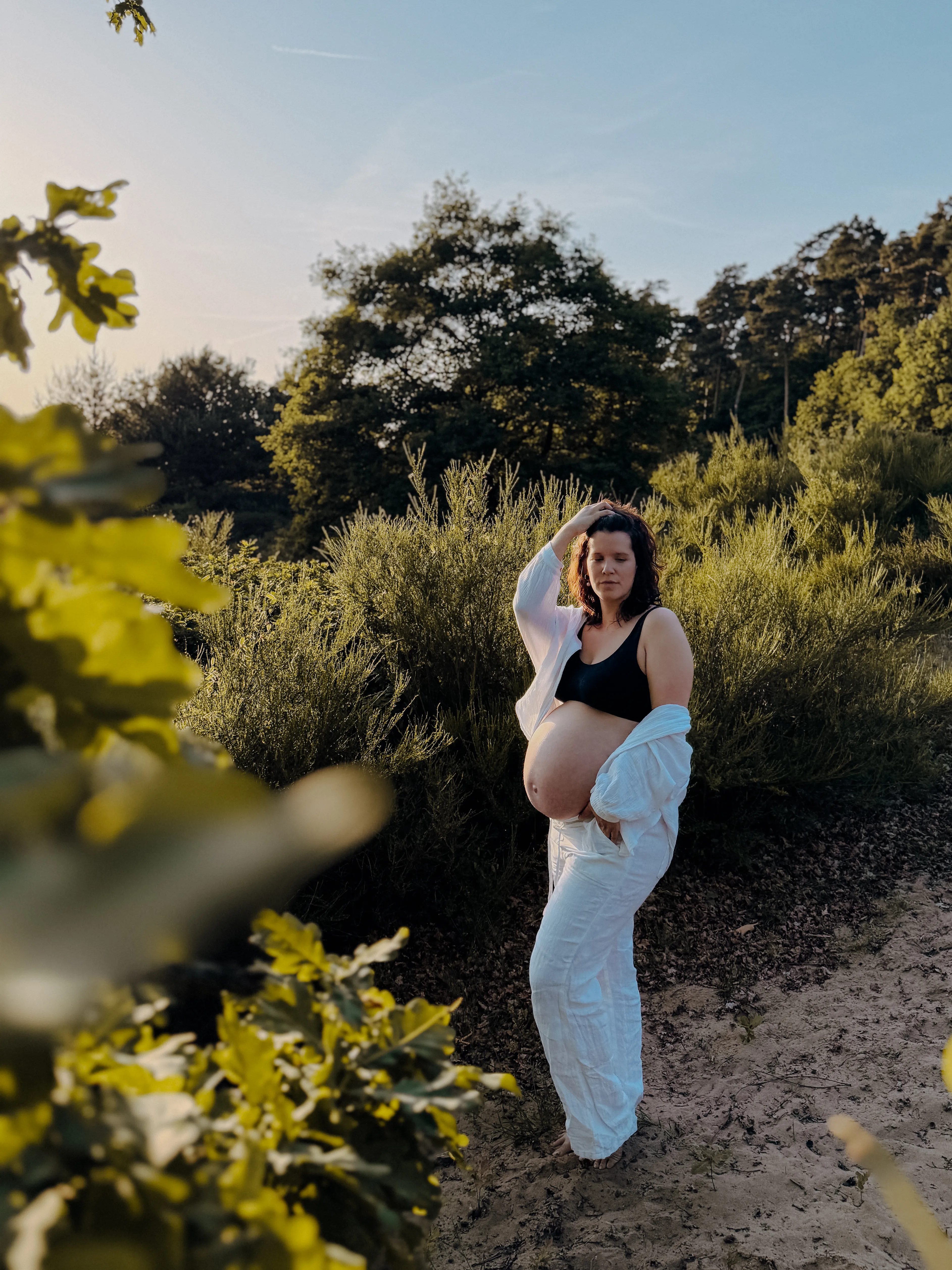 Beide Hände ruhen auf dem runden Babybauch, warmes Seitenlicht fällt durch die Vorhänge