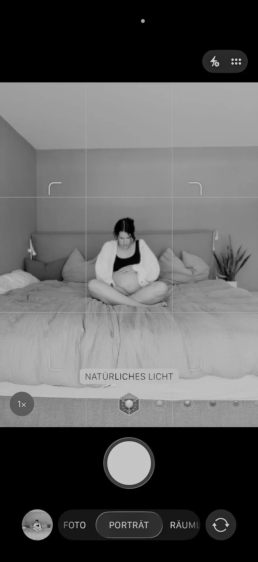 Schwangere macht in weichem Innenlicht ein Selbstporträt mit dem Smartphone