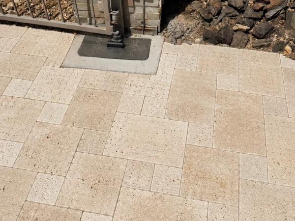 An overhead view of a light-colored travertine paver walkway with a varied pattern next to a metal gate.