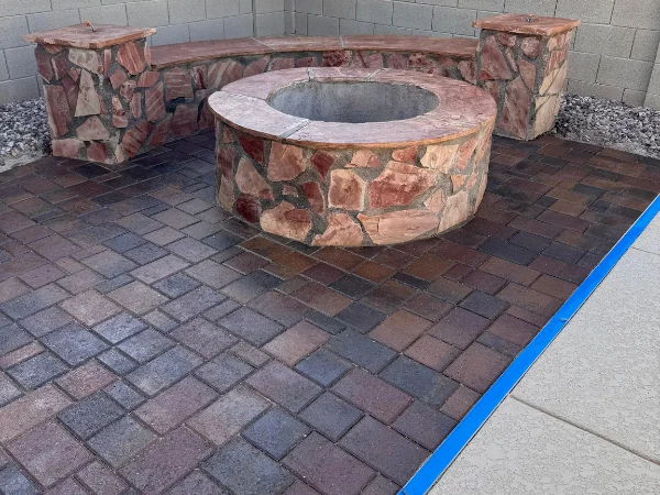 An outdoor patio features a stone fire pit area with a curved stone bench and matching low stone pillars.