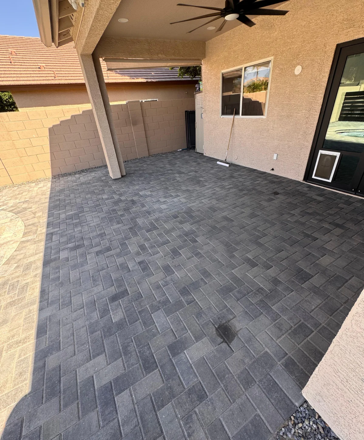 Modern luxury house exterior with gray stucco walls, black-framed windows and doors, stone accent column, and paved driveway under a clear blue sky.