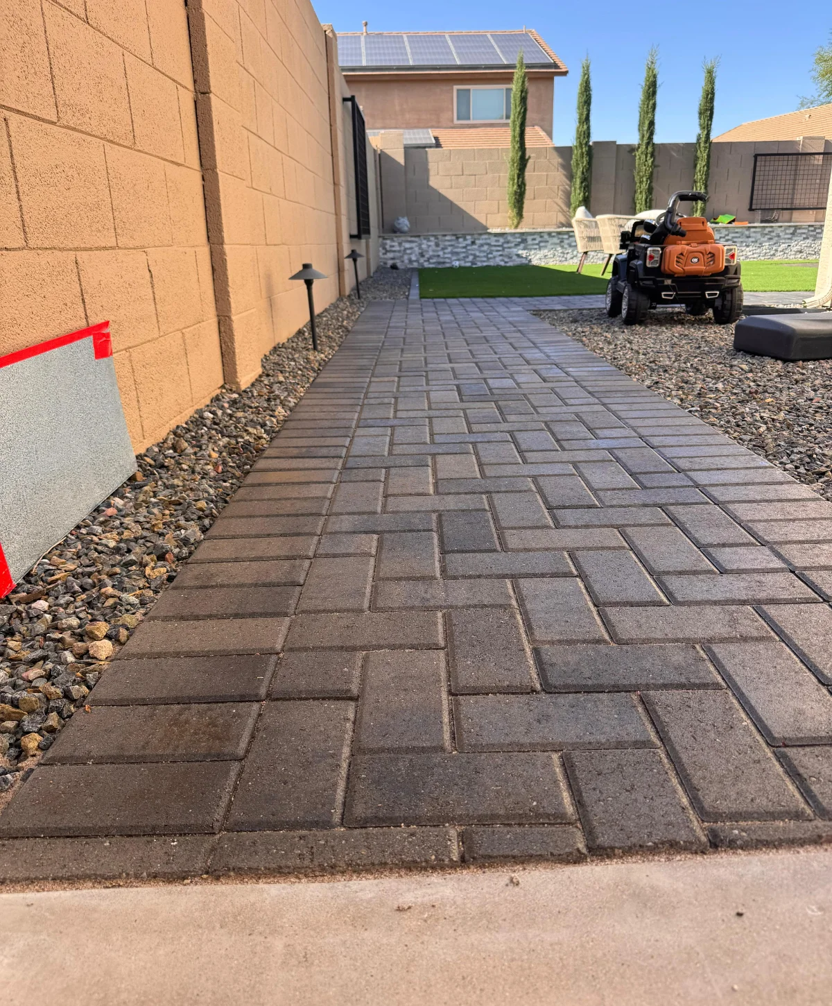 A long paver walkway with a herringbone pattern in a desert backyard, illuminated by the warm glow of the setting sun.