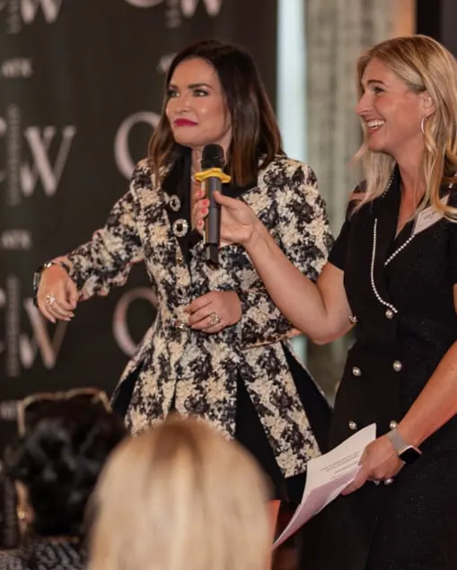 Joyce Toti holding a microphone for a smiling speaker in front of the CWL backdrop